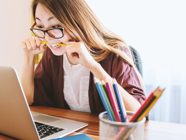 a girl that looks nervous biting a pencil in front of a laptop