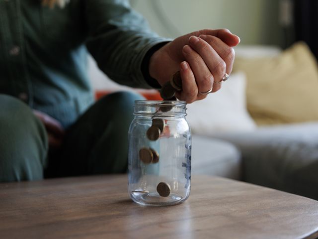 hand pouring coins into an empty jar