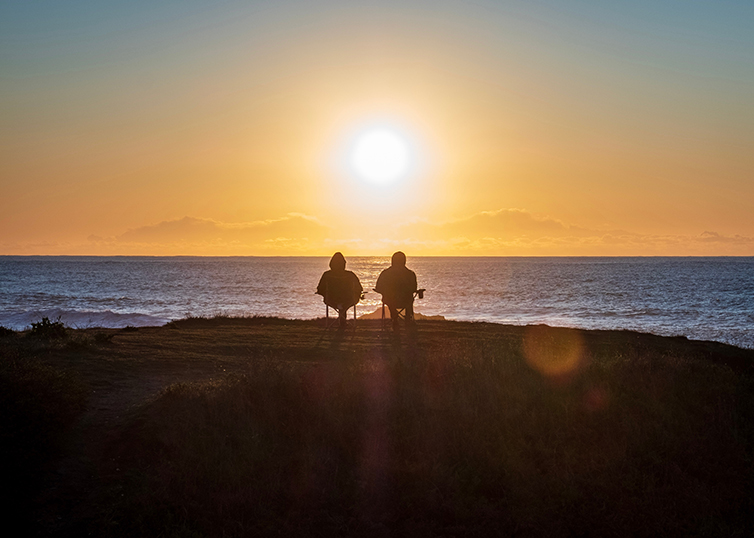 two people sitting on the beach watching the sunset