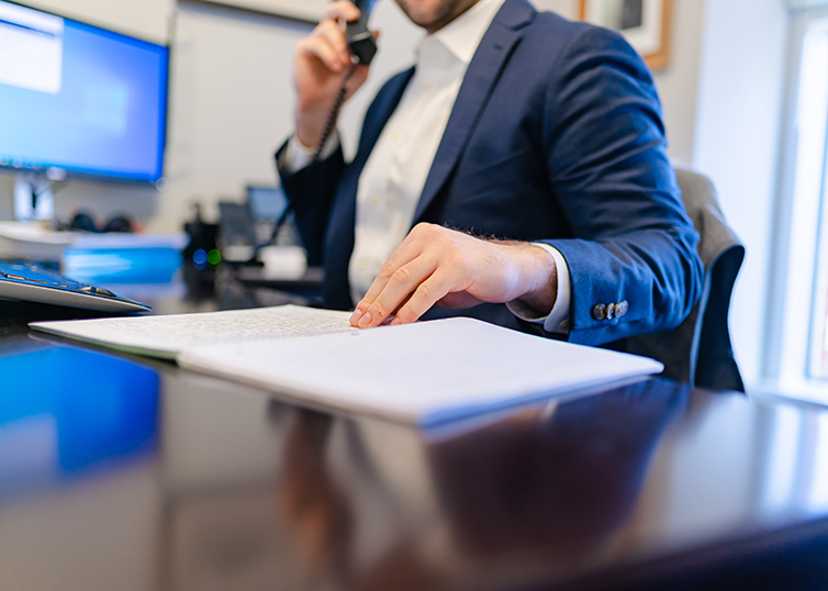 man in business suit at a desk on the phone with a hand on a notebook
