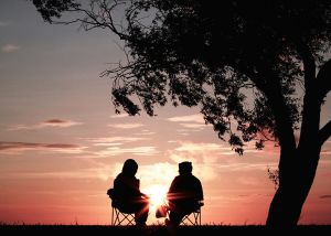 two people sitting in lawn chairs watching the sunset