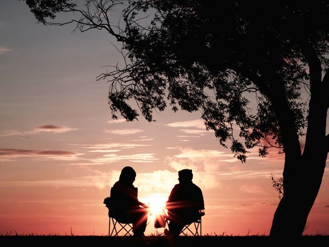 two people sitting in lawn chairs watching the sunset